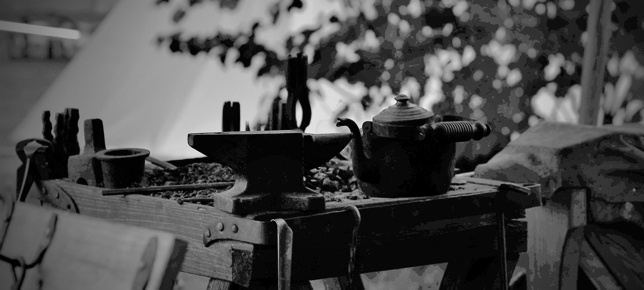 En vikingetida essa med stärd, tänger, hammare och en kaffekanna. et vikingetida tält och ett träd syns i bakrunden