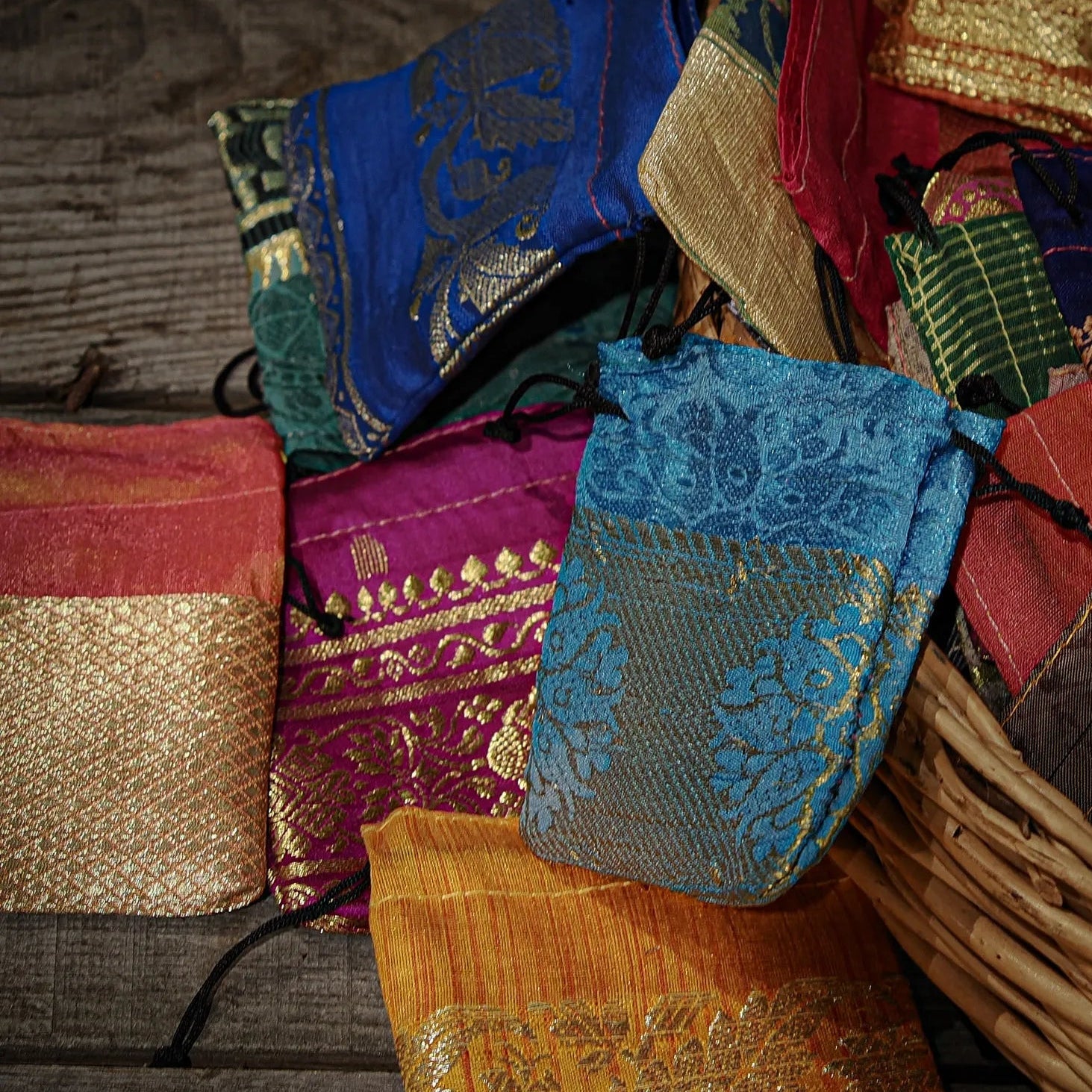 Färgglada tygpåsar i återvunnet sari-tyg med guldbroderier i korg på träbord