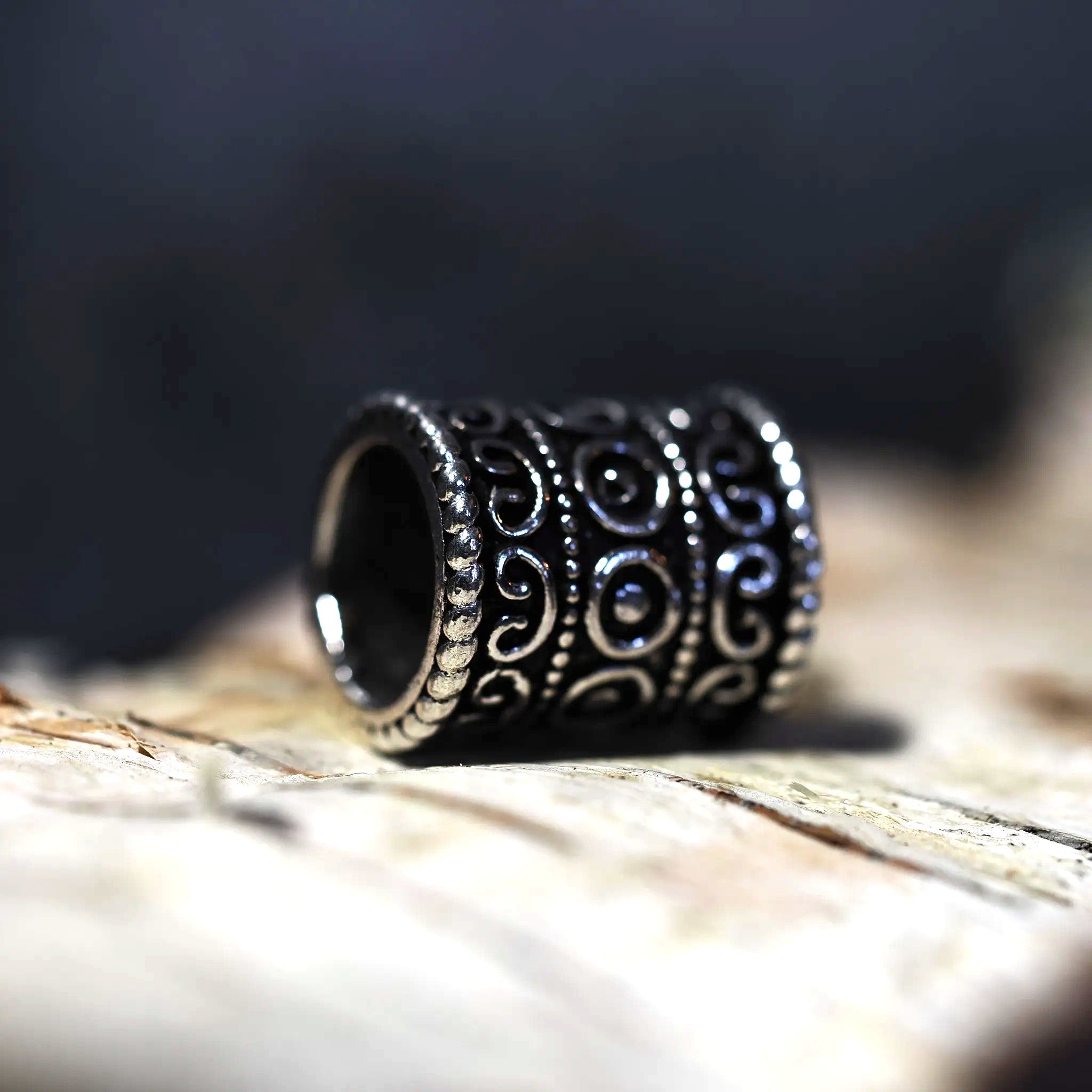 Närbild på skäggpärla Fimbula i mörkt stål med ornamentala spiralmönster, liggande på trä