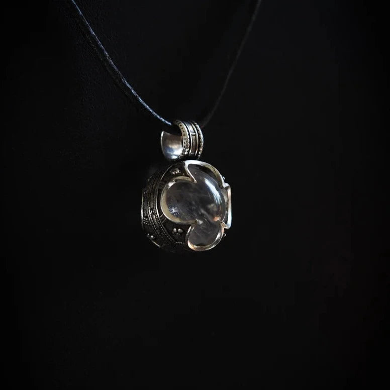 Silverhänge med bergkristall hängande i svart lädersnöre mot mörk bakgrund