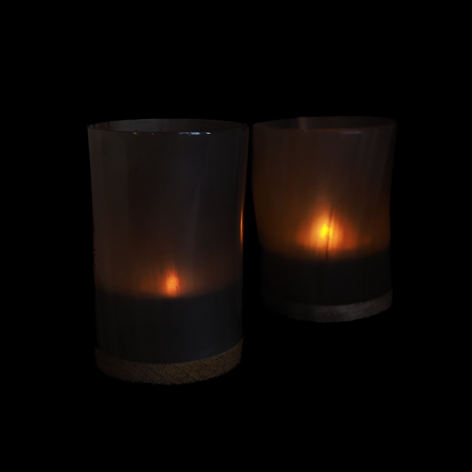 Två hornljuslyktor med tänd värmeljus i mörk miljö, som skapar ett varmt, hemmekosligt ljus genom hjärtformade hål i det organiska hornet.