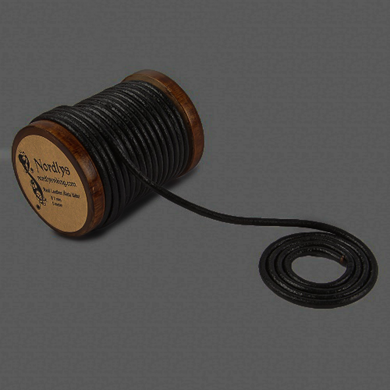 Svart 3mm läderband på träspole med utdraget band mot mörk bakgrund