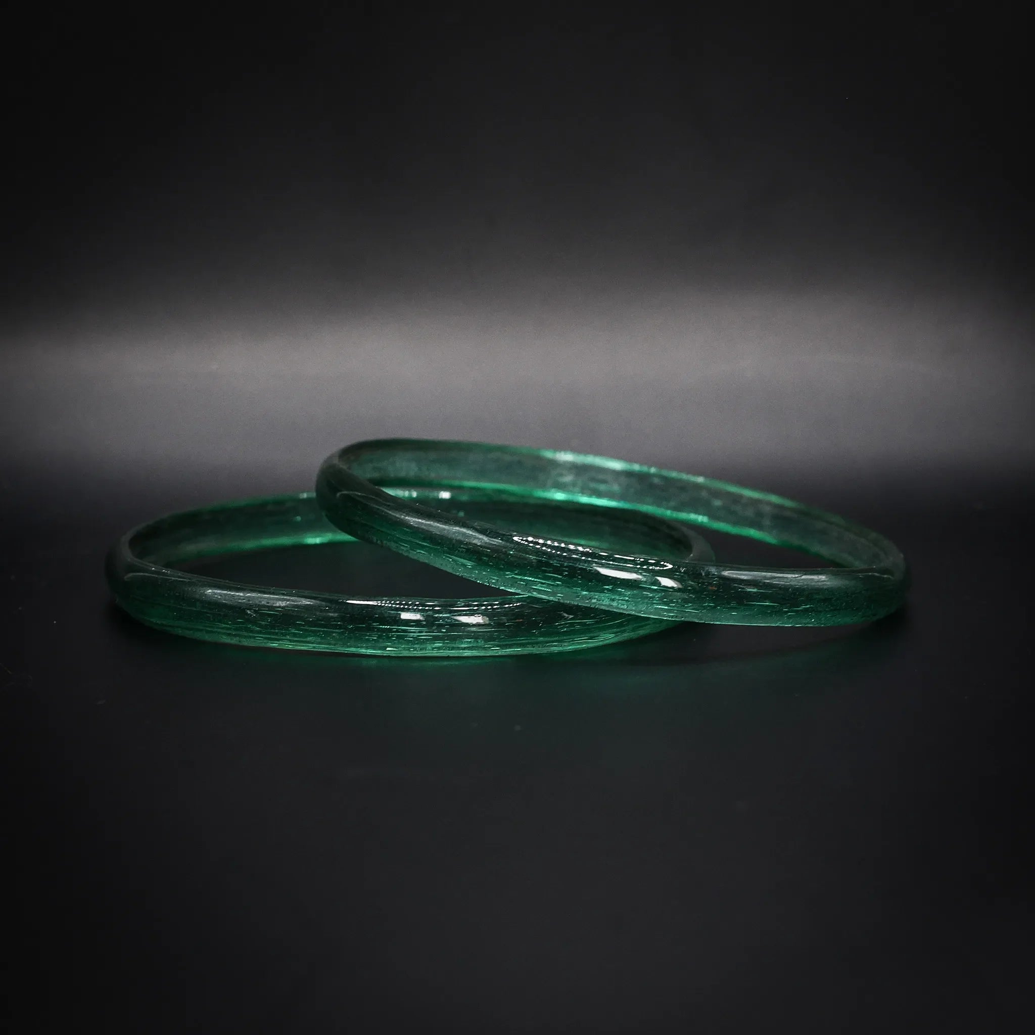 Par gröna glasarmband med genomskinlig struktur, vikingatida reproduktion mot mörk bakgrund