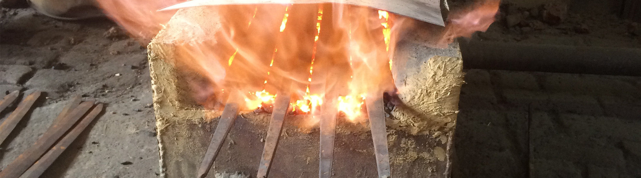 sword blades in a hardening oven. Flames are coming out and surrounding the metal