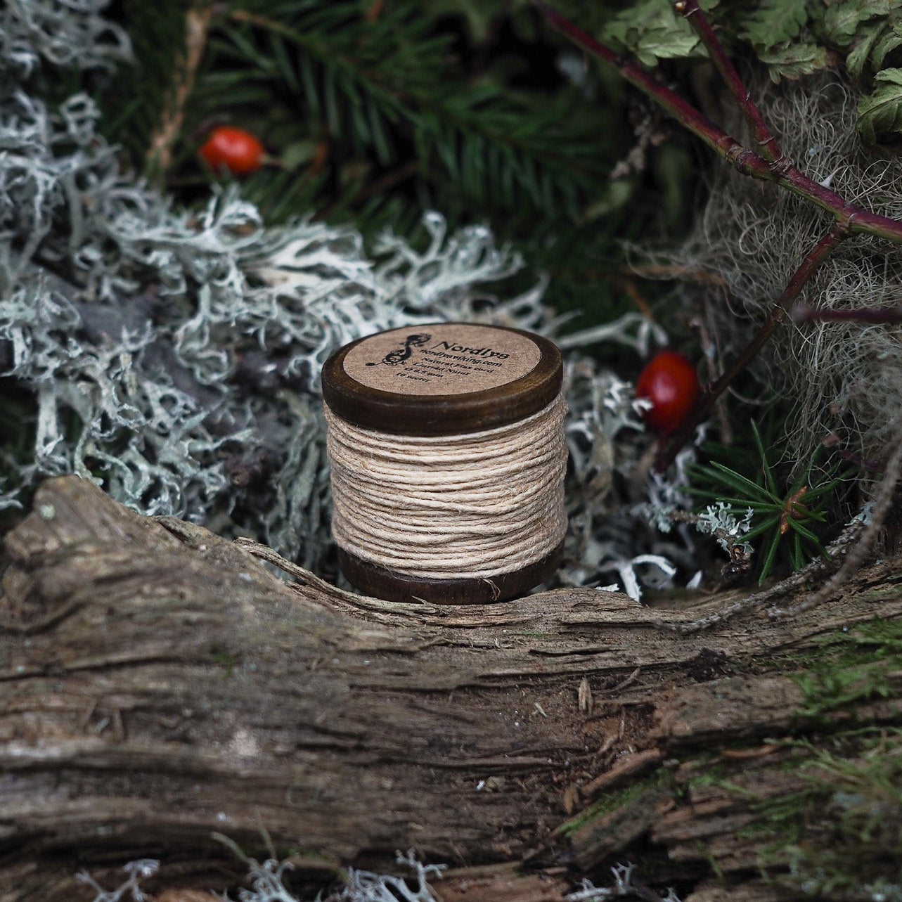 Liten träspole med naturfärgad linnetråd bland granris, renlav och nypon i vintermiljö