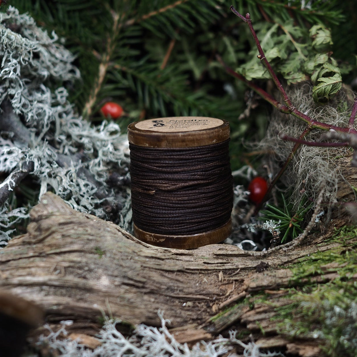 Brun polycord på rustik träspole bland granris, lav och nypon