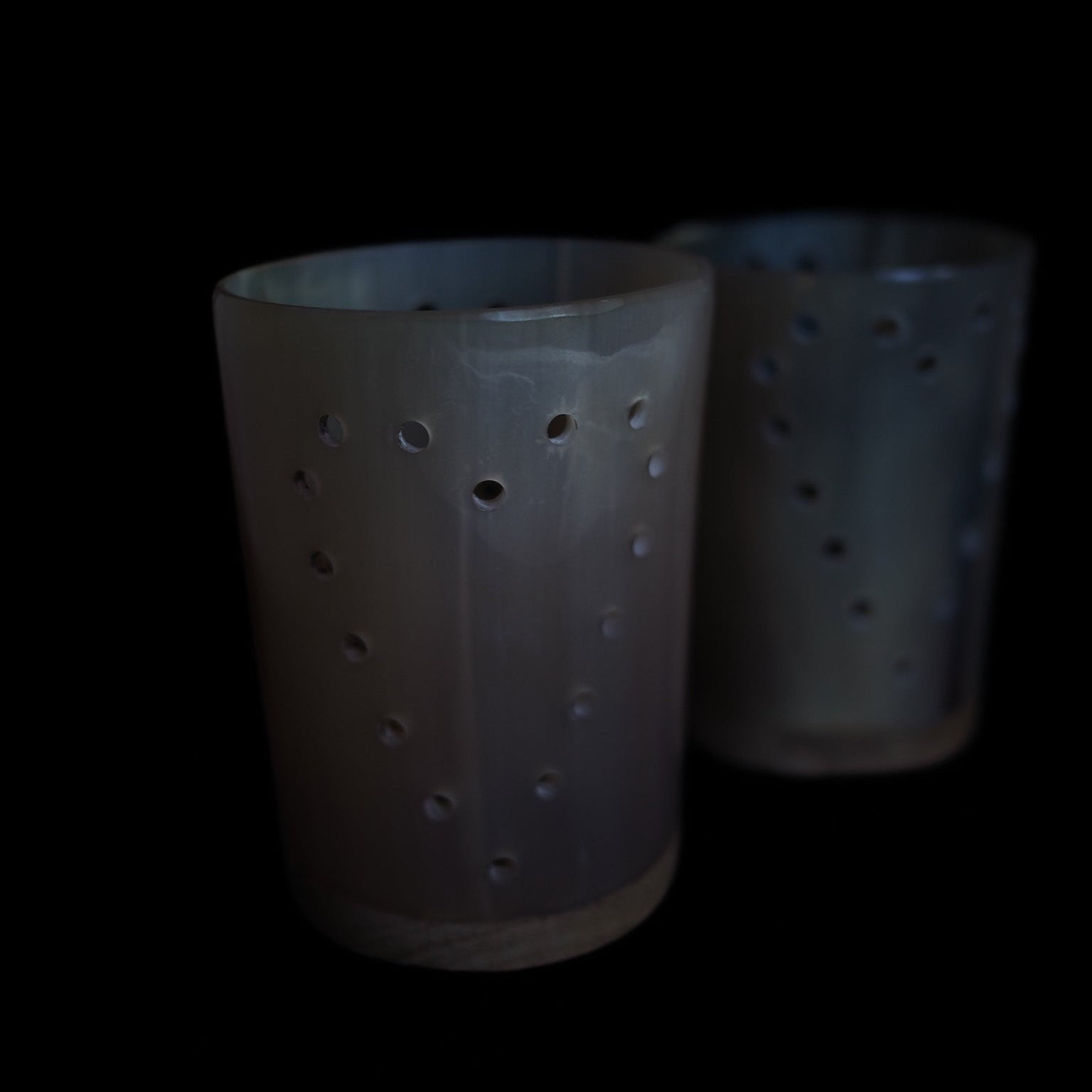 Två mörka hornlyktor med perforerat mönster utan ljus, mot svart bakgrund