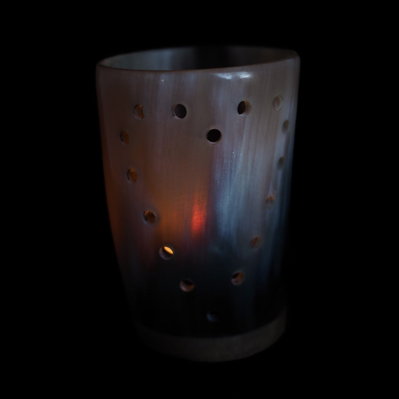 Hornlykta med perforerat mönster och tänt värmeljus, mjukt ljussken mot svart bakgrund