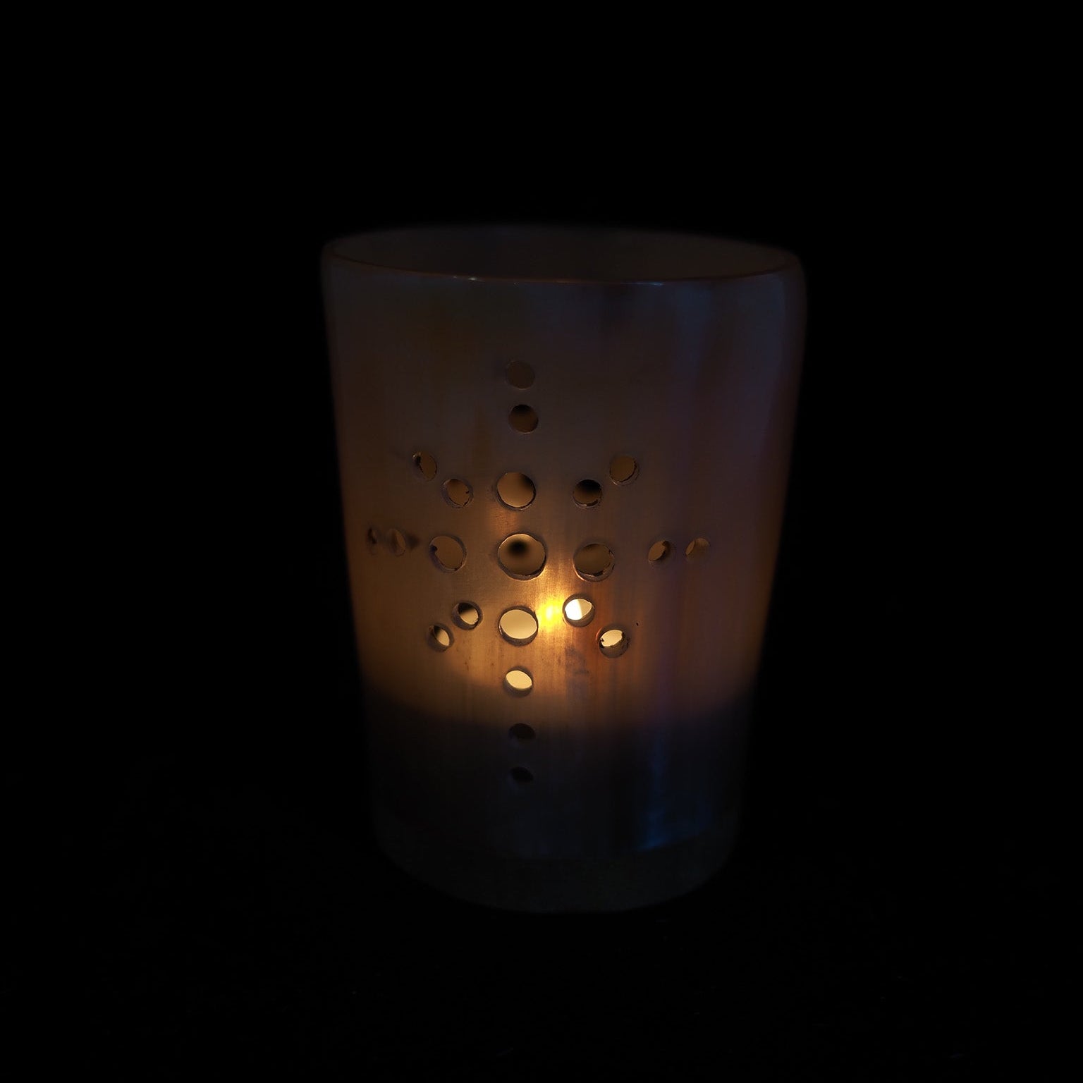 Ljus hornlykta med perforerat korsmönster och tänt värmeljus, varm glöd mot svart bakgrund